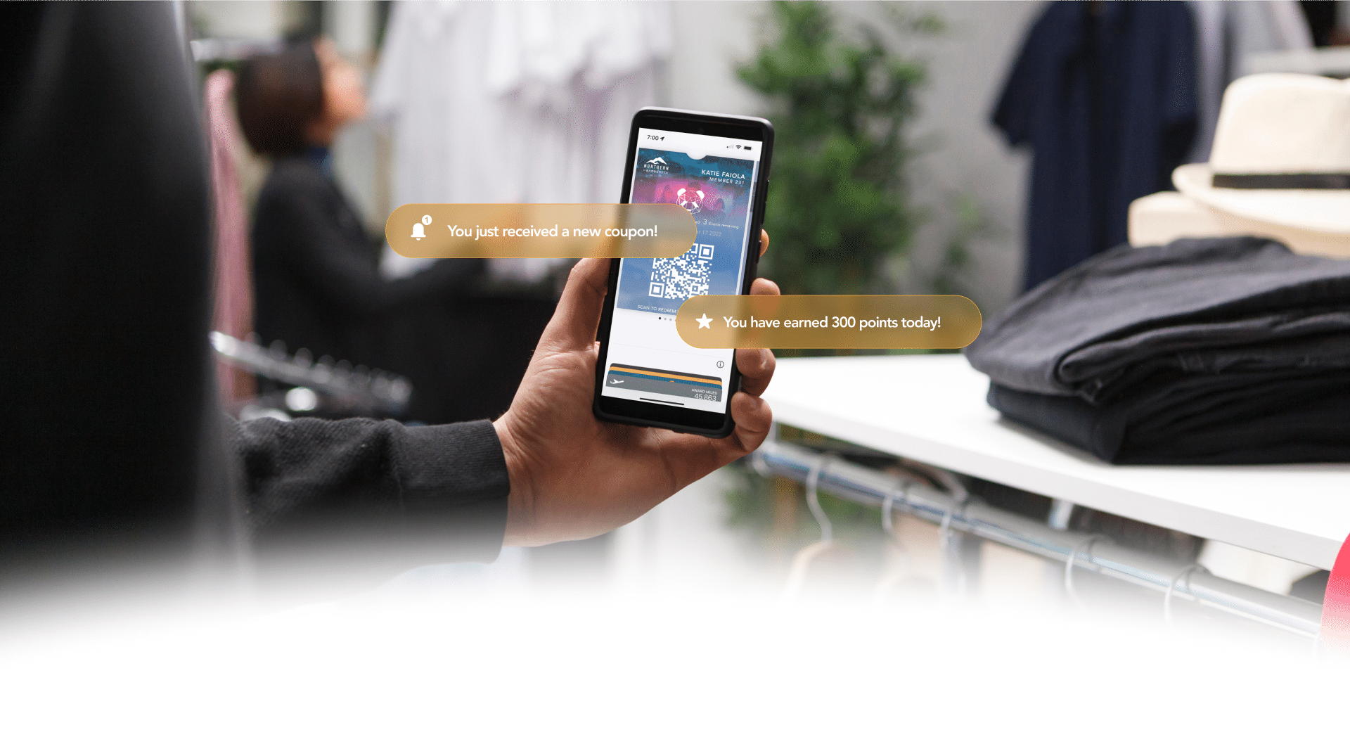 Customer holding a smartphone in a retail store displaying a mobile wallet pass with notifications for a new coupon and earned points.