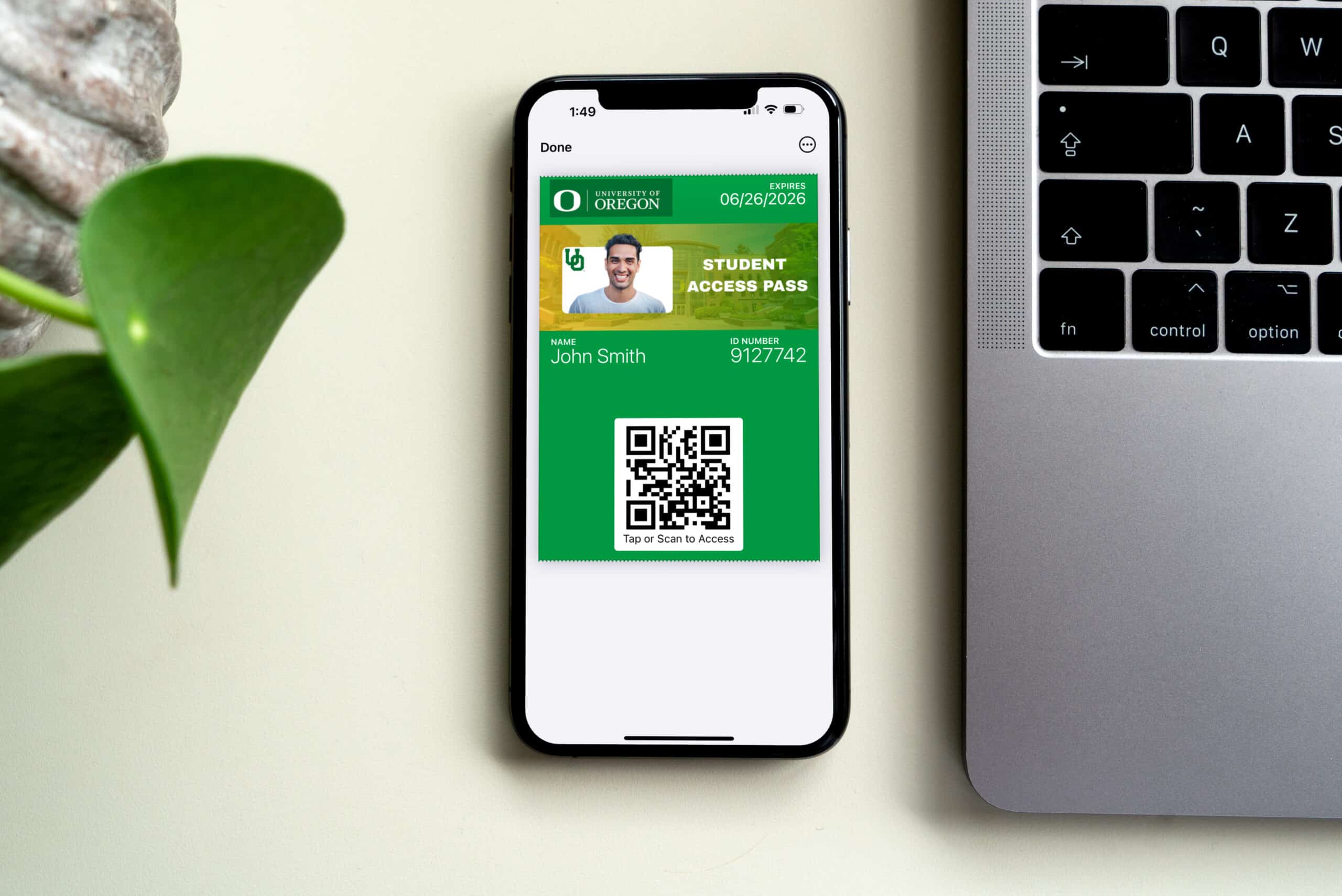 Smartphone displaying a digital student ID access pass with QR code next to a laptop on a desk.